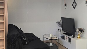 A loft bedroom with a bunk bed, a black sofa, a small round table, a TV on a white cabinet, and a wooden floor. - Sweet Escape. T1 BIS ROMANTIC (Bourg-lès-Valence)