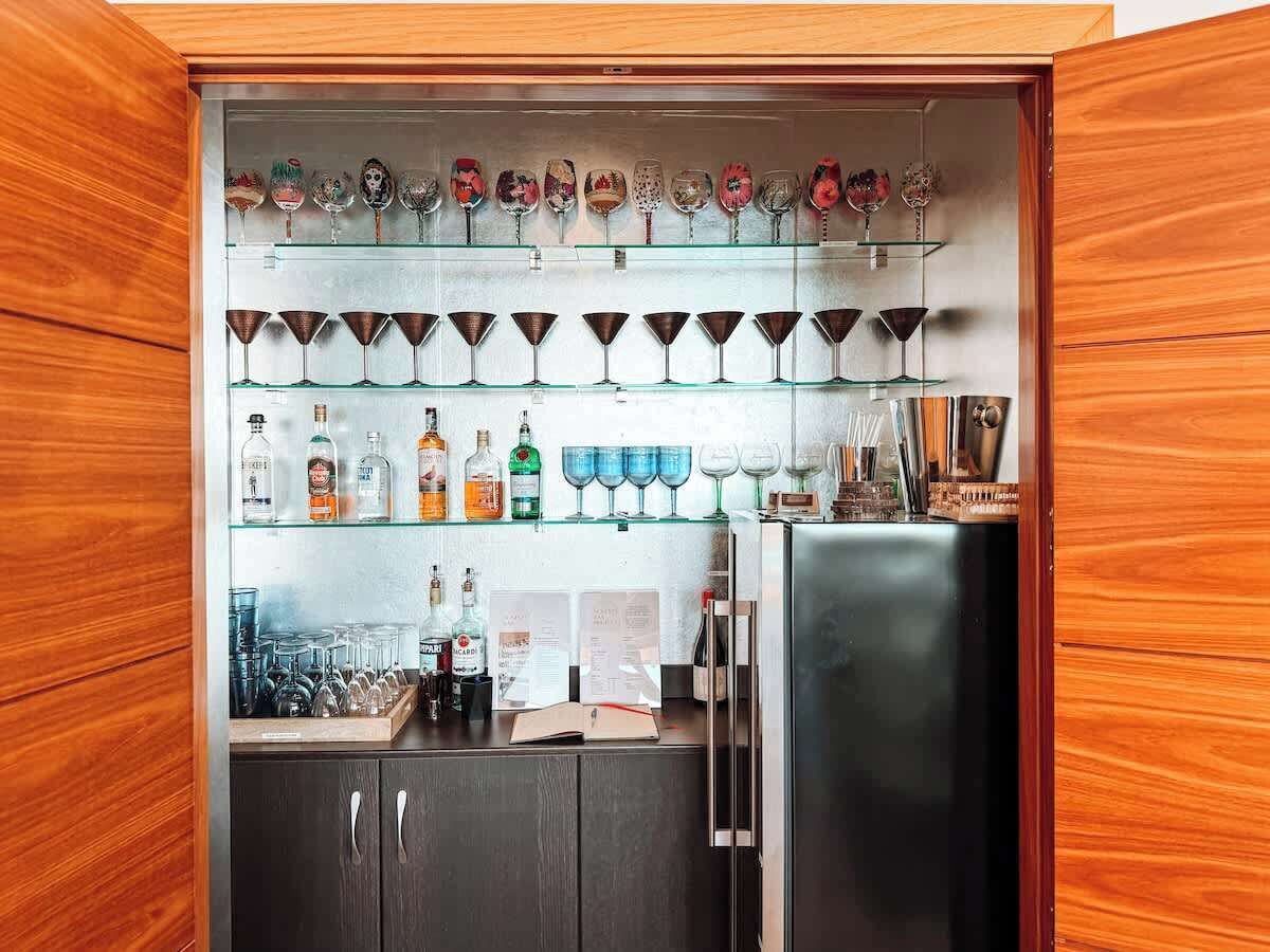 A bar area with shelves of liquor bottles, glasses, and a refrigerator.