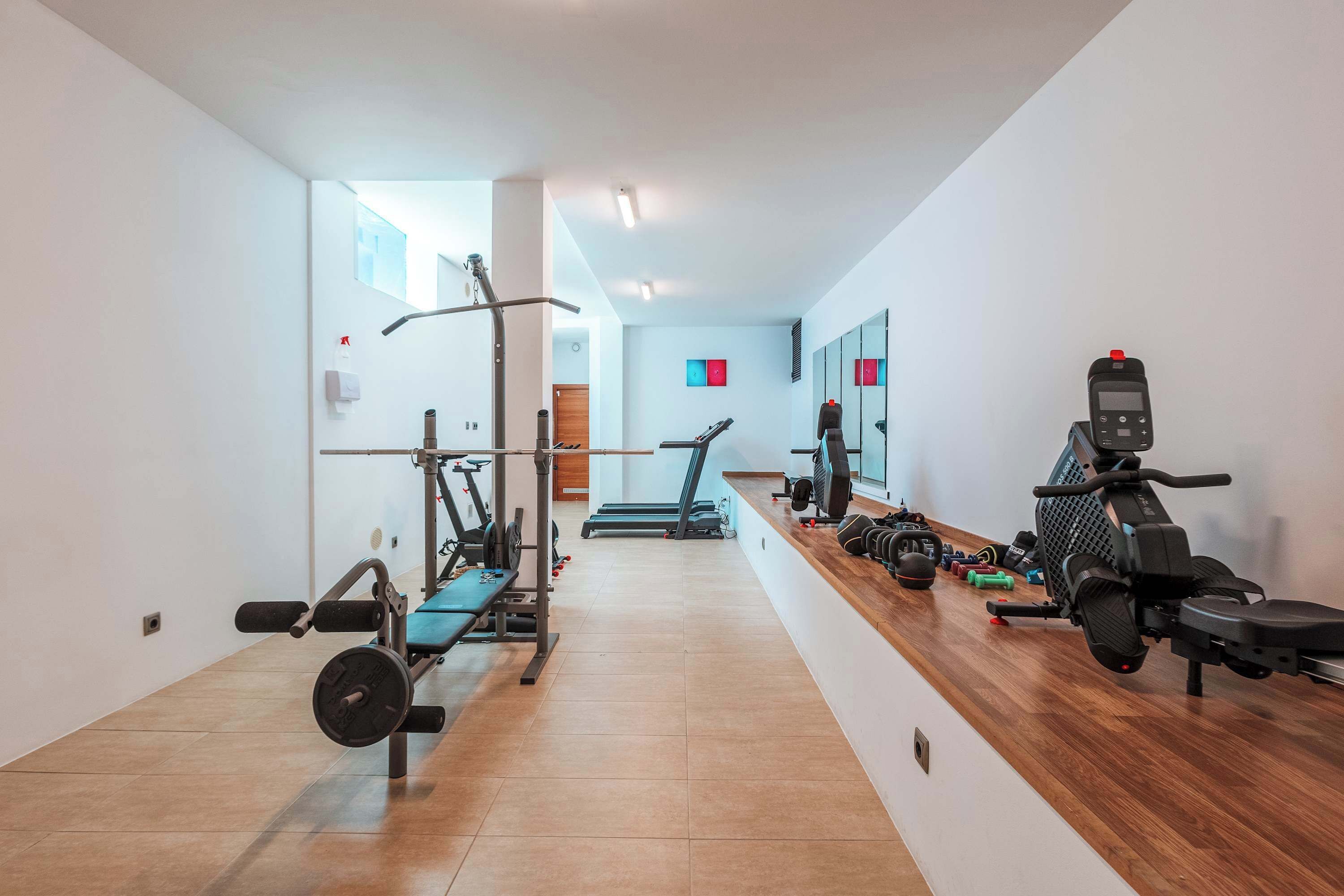 Une salle de sport moderne équipée de machines de cardio, de bancs de musculation et d’un comptoir en bois où sont rangés des haltères.