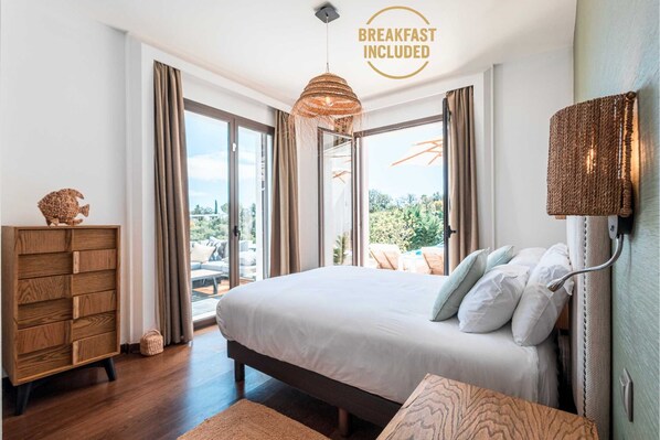 Une chambre avec un grand lit, une commode en bois et une vue sur l’extérieur.