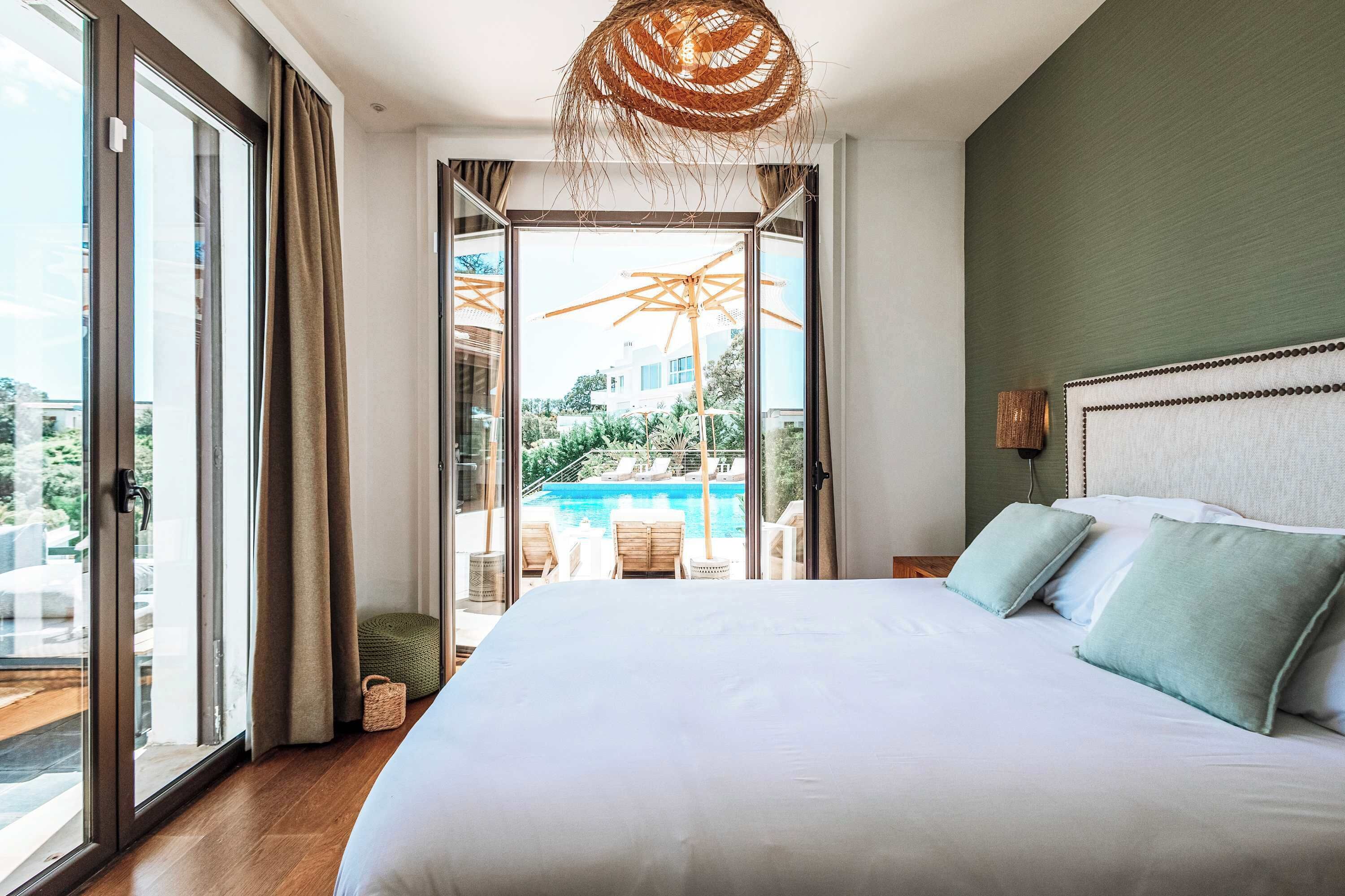 A bedroom with a large bed, a view of a swimming pool, and a balcony.