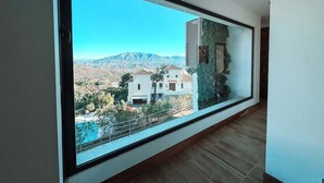A modern interior with a large window offering a view of a mountainous landscape and residential buildings. - Poolside Room - Deluxe Boutique B&B Ojén/Marbella (Ojén)