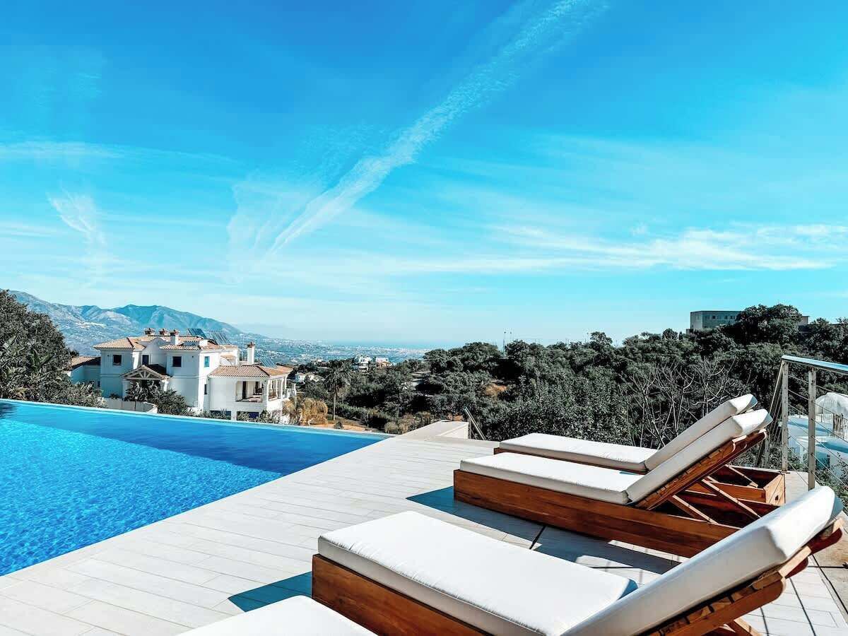 A poolside area with lounge chairs, a clear blue sky, and a view of a mountainous landscape.