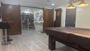 A billiards table in a room with wooden flooring, a bookshelf, and a dartboard. - Turtle cove: Perfect Cozy Oasis in SWFL with Pool, Hot Tub & More! (Fort Myers)