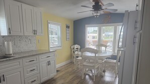 A kitchen with white cabinets, a marble countertop, and a dining area with white chairs and a table. - Turtle cove: Perfect Cozy Oasis in SWFL with Pool, Hot Tub & More! (Fort Myers)