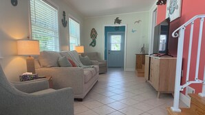 A living room with a sofa, armchair, and a lamp. There is a door with a window and a wall with decorative elements. - Turtle cove: Perfect Cozy Oasis in SWFL with Pool, Hot Tub & More! (Fort Myers)