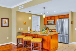 Una cocina con armarios de madera, un refrigerador de acero inoxidable y una zona de asientos con taburete de bar.