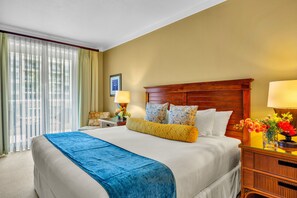 Habitación de hotel con una cama grande, cabecera de madera, mesita de noche con lámpara y vistas al exterior a través de cortinas traslúcidas.