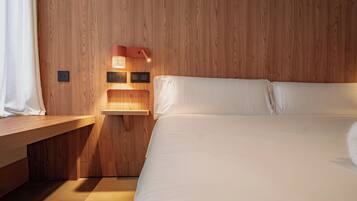 A bedroom with a wooden headboard, a bedside table, a bed with white bedding, and a wall-mounted light fixture.