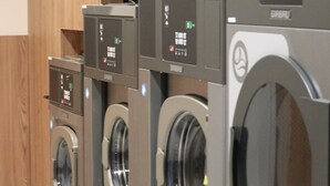 A row of front-loading washing machines with control panels, arranged in a commercial setting. - CASA ROMA Hostel Boutique (Tarragona)