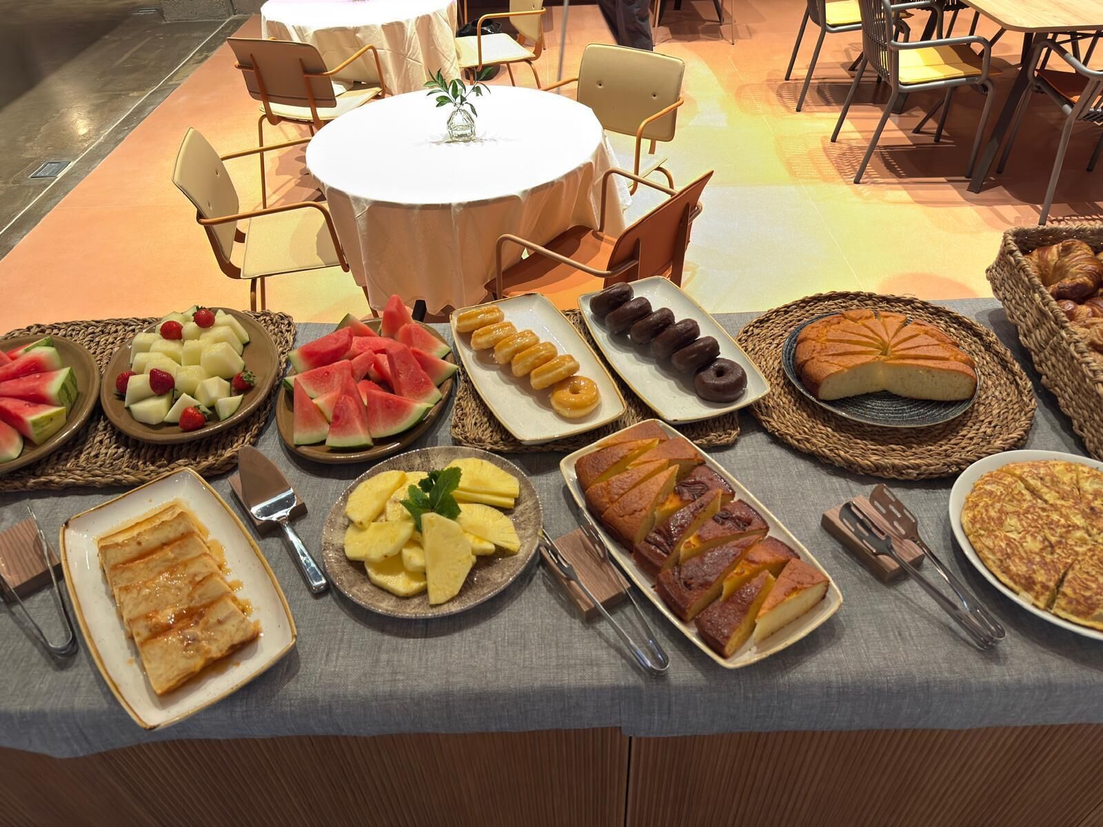 A buffet table with various food items including watermelon, pineapple, pastries, and donuts.