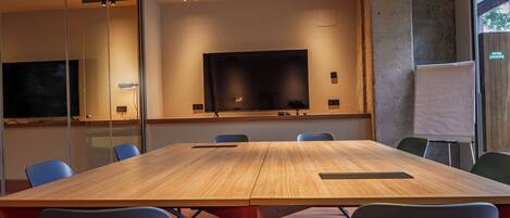 Un salón de conferencias con una gran mesa, sillas, una pantalla de televisión y una pizarra.