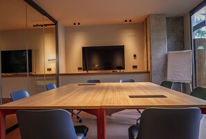 A conference room with a large table, chairs, a TV screen, and a whiteboard.
