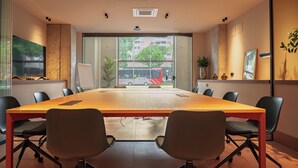 A conference room with a long table, chairs, a whiteboard, and large windows with a view of buildings and trees. - CASA ROMA Hostel Boutique (Tarragona)