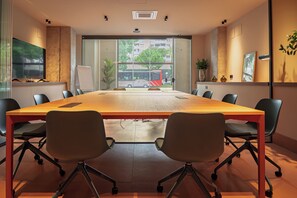 Un salón de conferencias con una larga mesa, sillas, una pizarra y ventanas amplias que dan a vistas de edificios y árboles.