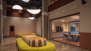 A modern interior with a curved yellow seating area, a glass partitioned room with a dining table and chairs, and pendant lighting. - CASA ROMA Hostel Boutique (Tarragona)