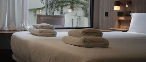 A hotel room with a bed, a window with curtains, a bedside table with a lamp, and a view of trees outside.