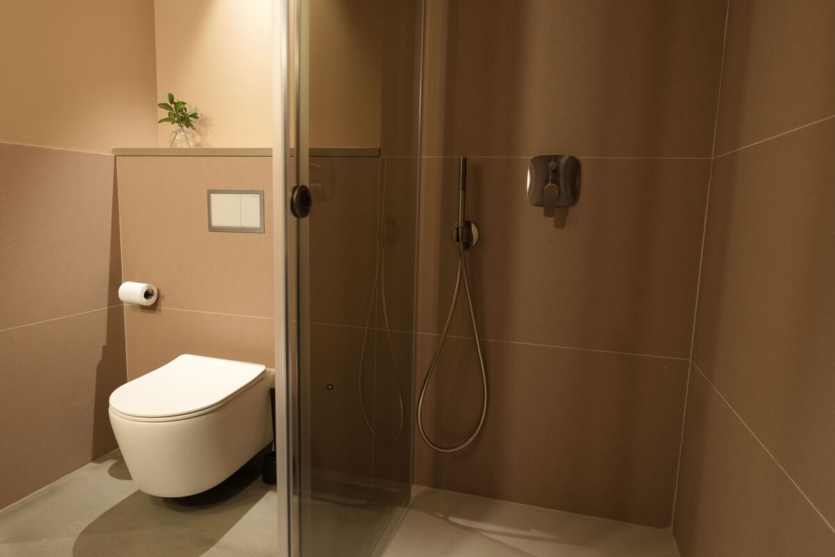 A modern bathroom with a toilet, shower, and a small plant on the wall.