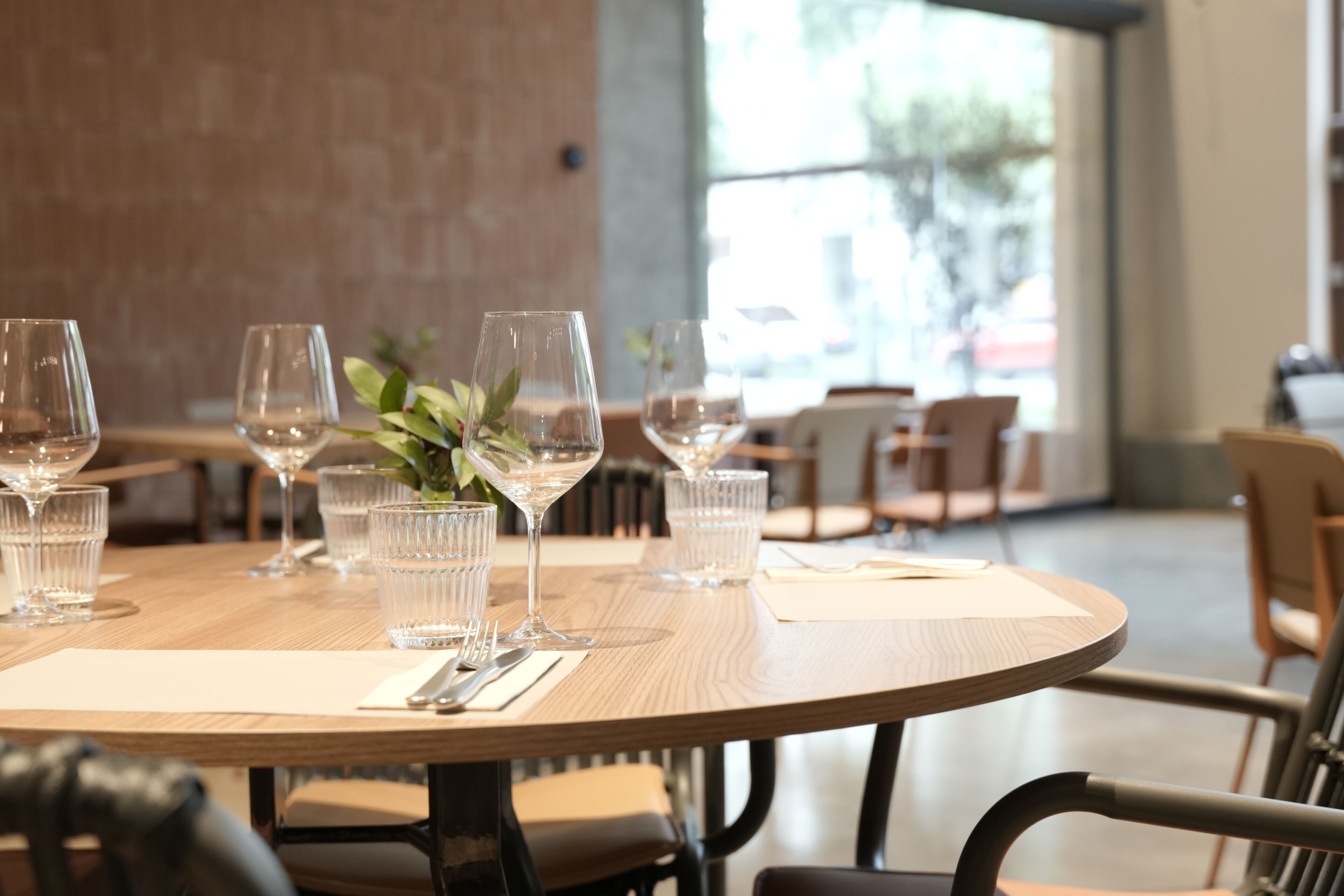 A dining table set with wine glasses, a plant, and cutlery.