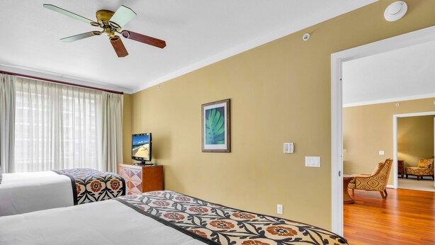 Une chambre d’hôtel avec deux lits, un ventilateur de plafond, une télévision et un tableau encadré au mur.