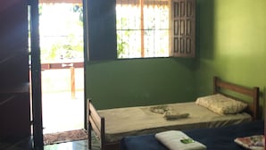Una habitación con dos camas, una puerta de madera, una ventana con barrotes y piso de baldosas.