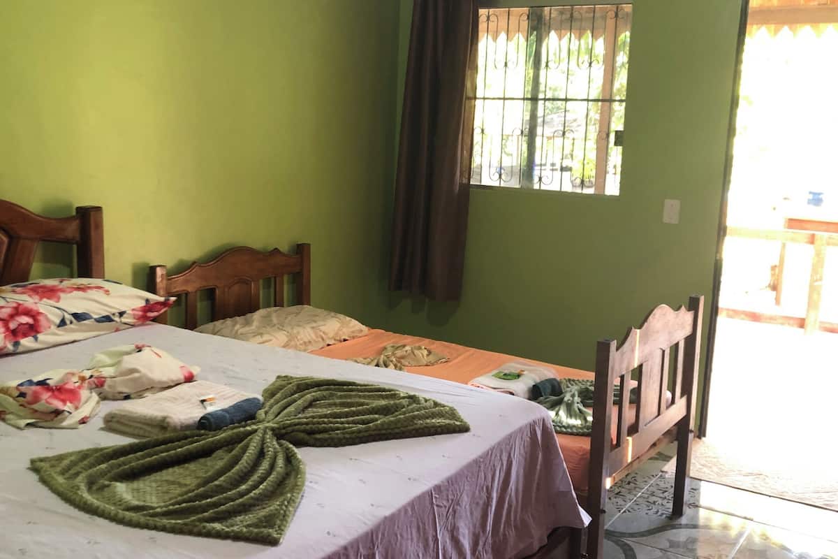 A bedroom with a bed, wooden headboard, green walls, a window with bars, and a tiled floor.