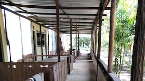 A covered corridor with wooden benches and brick walls, leading to an open area with greenery.