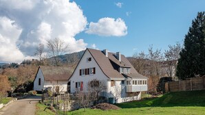 A two-story house with a sloped roof, a visible chimney, and a front porch. - Alte Zainschmiede Holiday Apartment – Pure Peace and Relaxation (Müllheim im Markgräflerland)