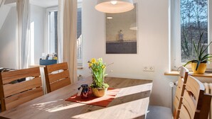 A dining area with a wooden table, chairs, a hanging light fixture, a potted plant, and a window with a view of trees. - Alte Zainschmiede Holiday Apartment – Pure Peace and Relaxation (Müllheim im Markgräflerland)