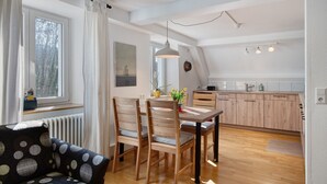 A modern kitchen with wooden cabinets, a dining table with chairs, and a window with curtains. - Alte Zainschmiede Holiday Apartment – Pure Peace and Relaxation (Müllheim im Markgräflerland)