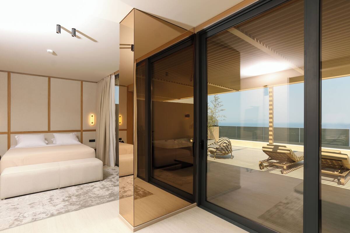 Un dormitorio moderno con una cama grande, una puerta de vidrio que da a un balcón con sillones de descanso.