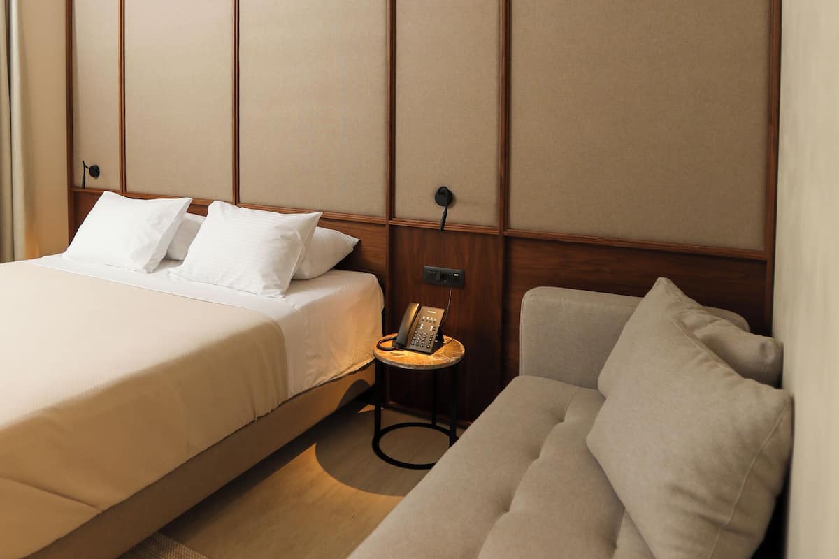 Una habitación de hotel con una cama, un sofá y un teléfono junto a la cama.