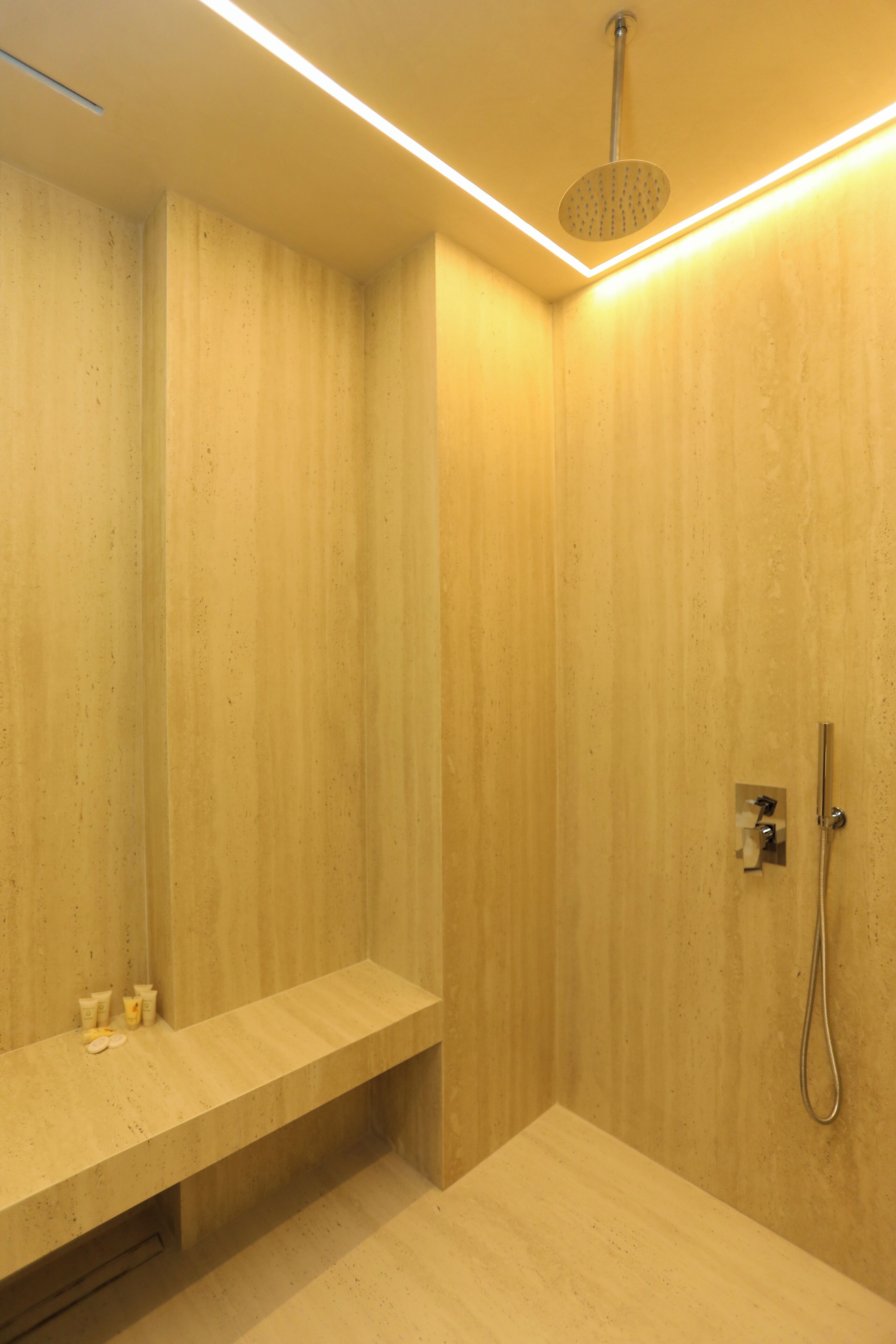 A modern shower area with a bench, a handheld showerhead, and a wall-mounted faucet.