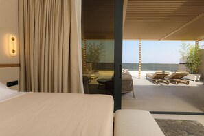 Quarto de hotel moderno com uma cama grande, uma varanda com espreguiçadeiras e vista para o mar.
