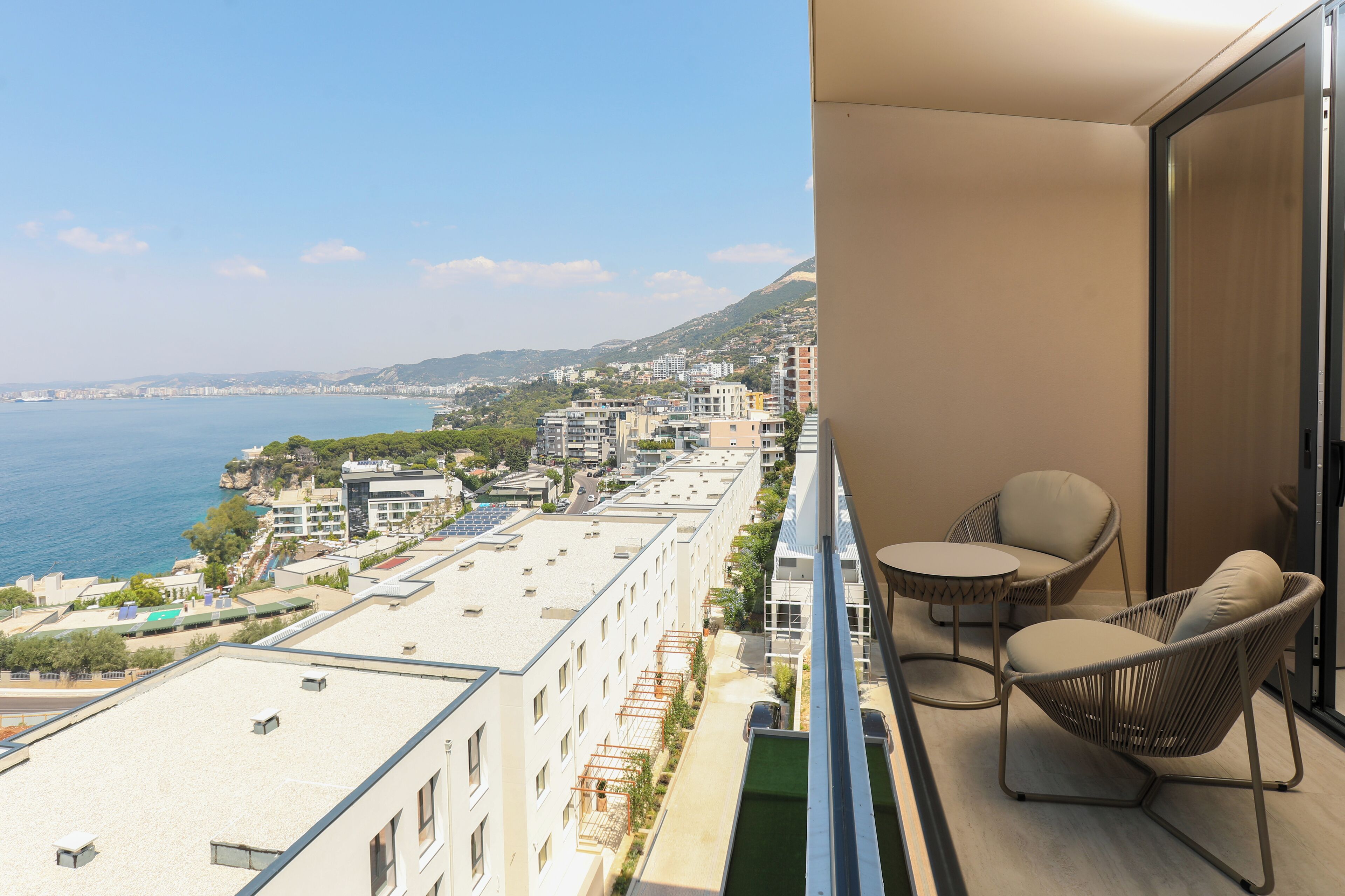 A balcony with a view of the sea and cityscape, furnished with two chairs and a small table.