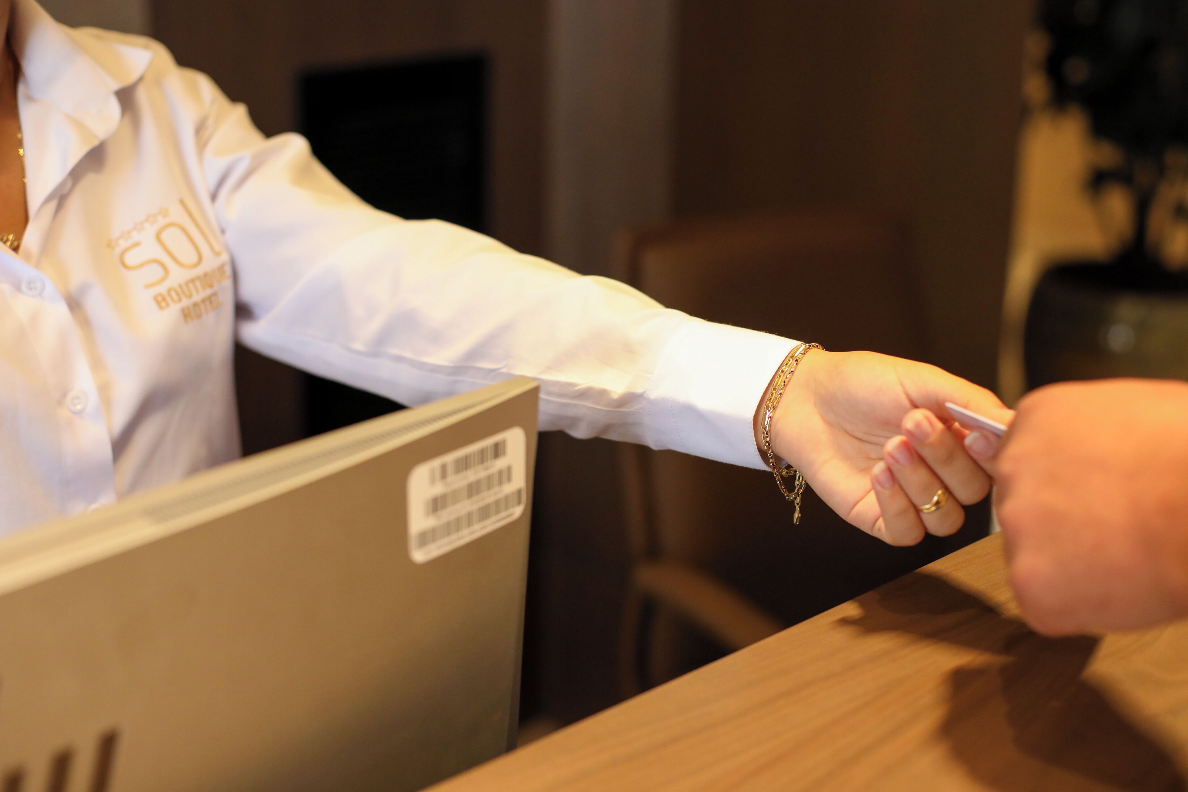 Une personne portant une chemise blanche avec l’inscription « 50 Boutique Hotel », qui tend une carte à une autre personne au comptoir d’accueil.