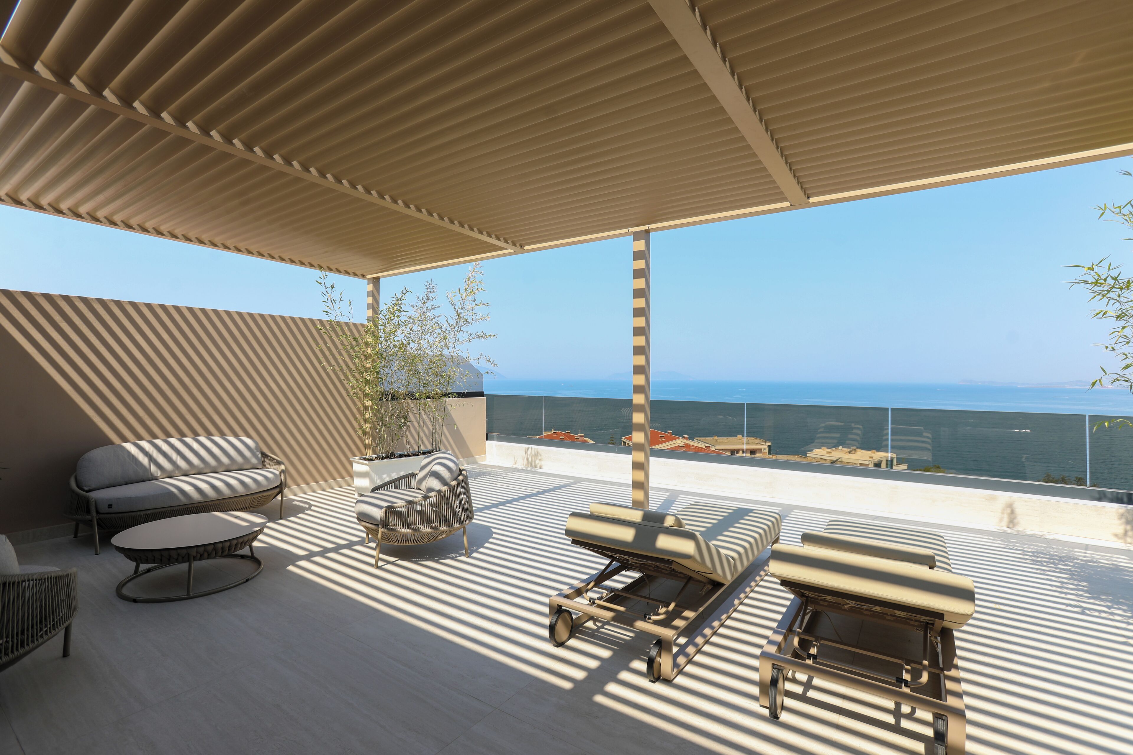 A rooftop terrace with a view of the sea, featuring a sofa, lounge chairs, and a dining table.