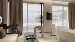 Une chambre d’hôtel moderne dotée d’une grande fenêtre, d’un téléviseur à écran plat, d’un canapé, d’un fauteuil, d’une baignoire et d’une table basse.