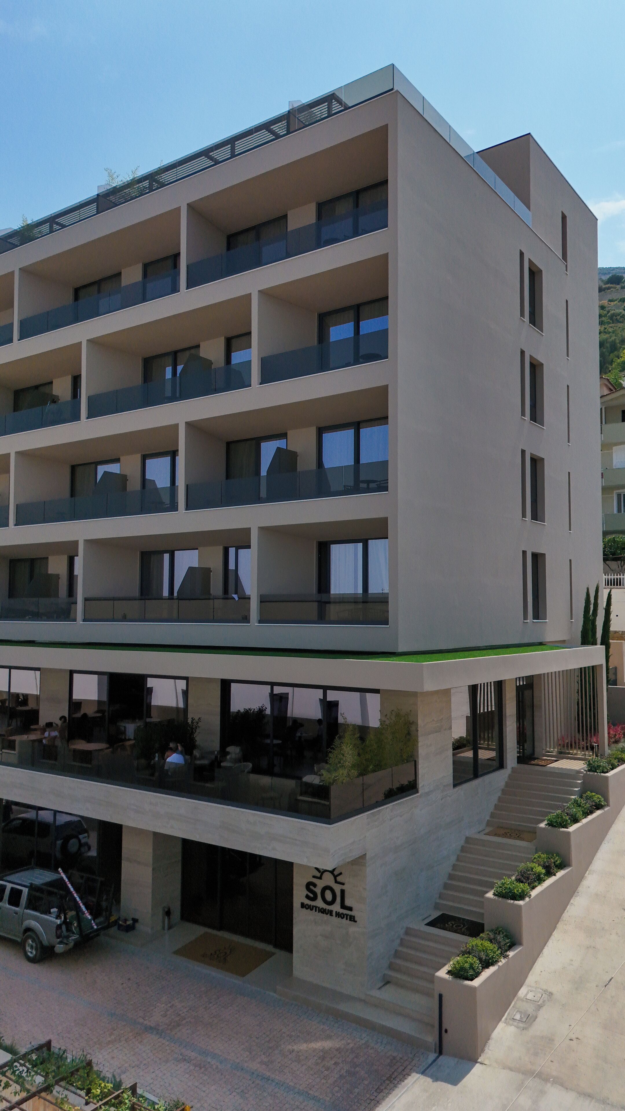 A multi-story hotel with a flat facade, balconies, and a ground-level cafe area.
