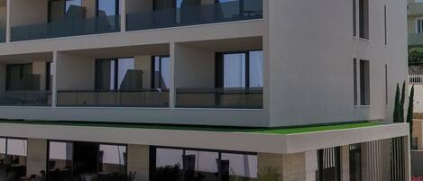 A multi-story hotel with a flat facade, balconies, and a ground-level cafe area.