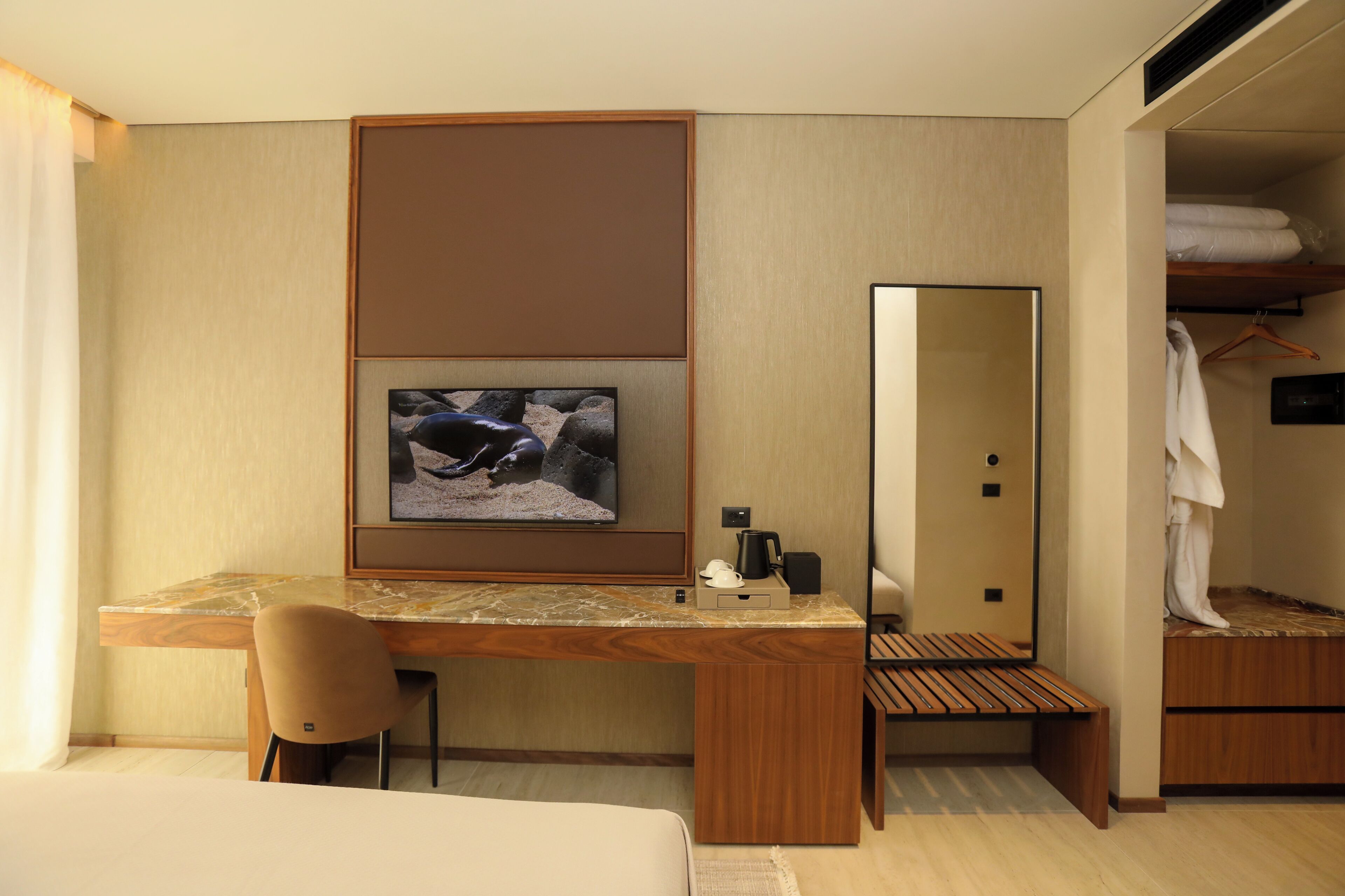 A hotel room with a wooden desk, a television mounted on the wall, a mirror, and a walk-in closet.