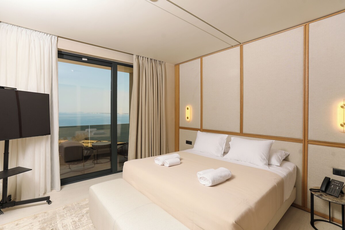 A hotel room with a large bed, a TV, a bedside table, and a view through a glass door.