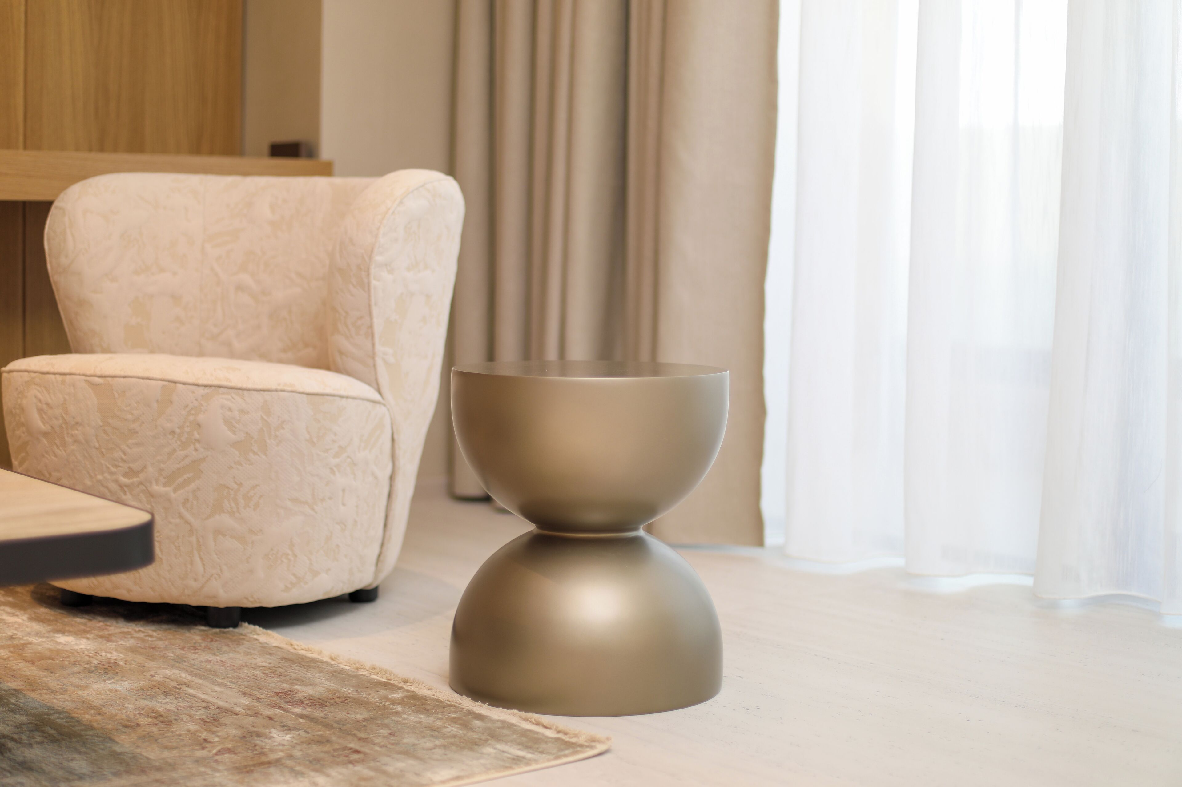 A modern living room with a plush armchair, a minimalist side table, and sheer curtains.