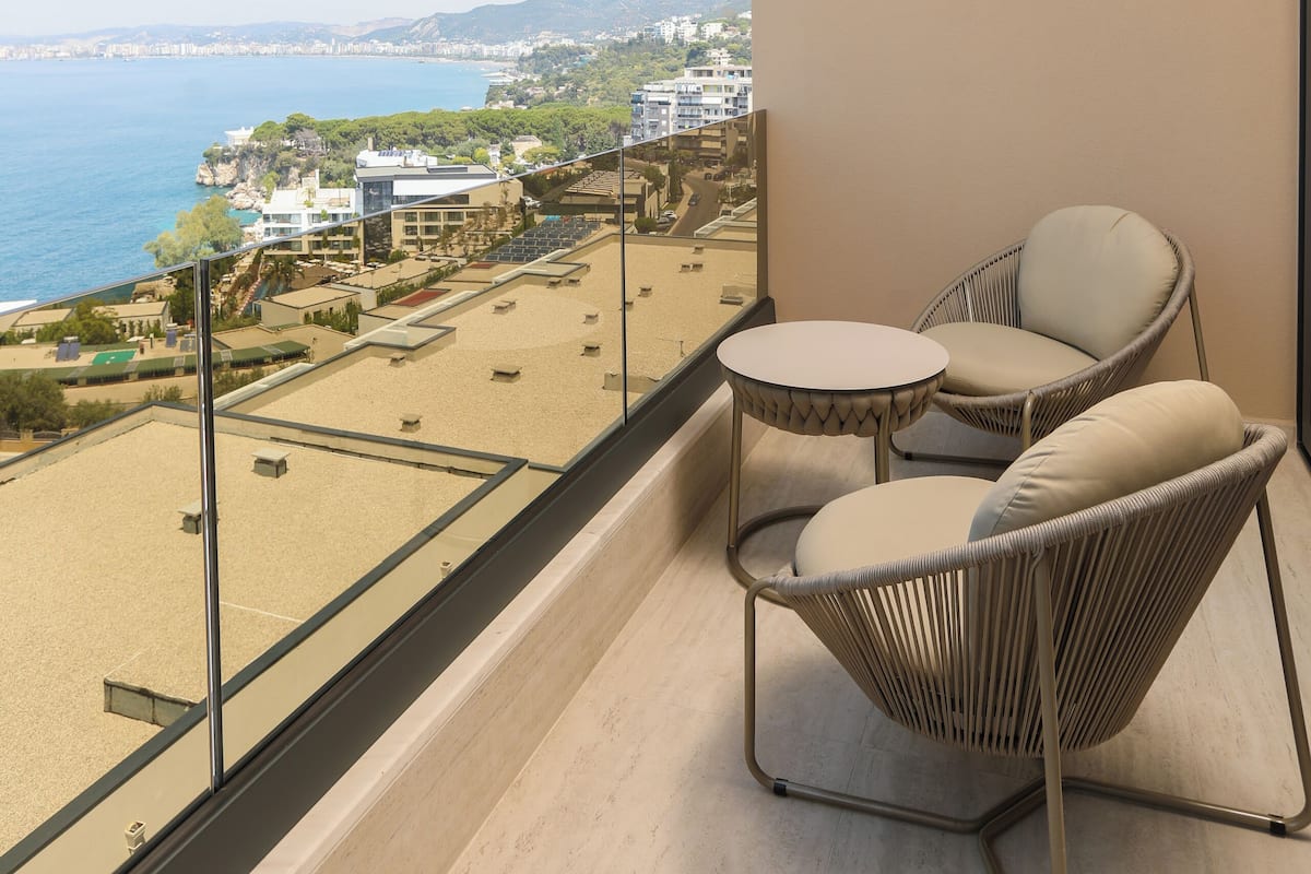 Un balcón con vistas al mar y edificios, con dos sillones de mimbre y una pequeña mesa.