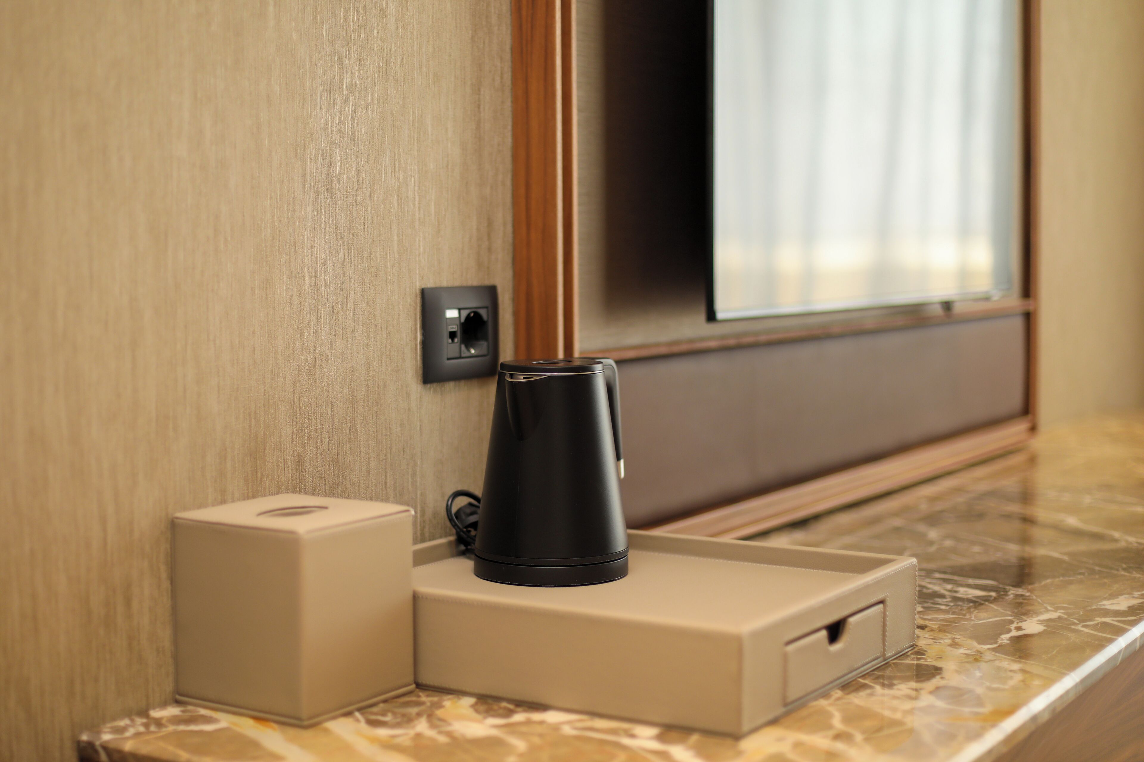 A modern hotel room with a marble countertop, a black electric kettle, and a beige charging station.