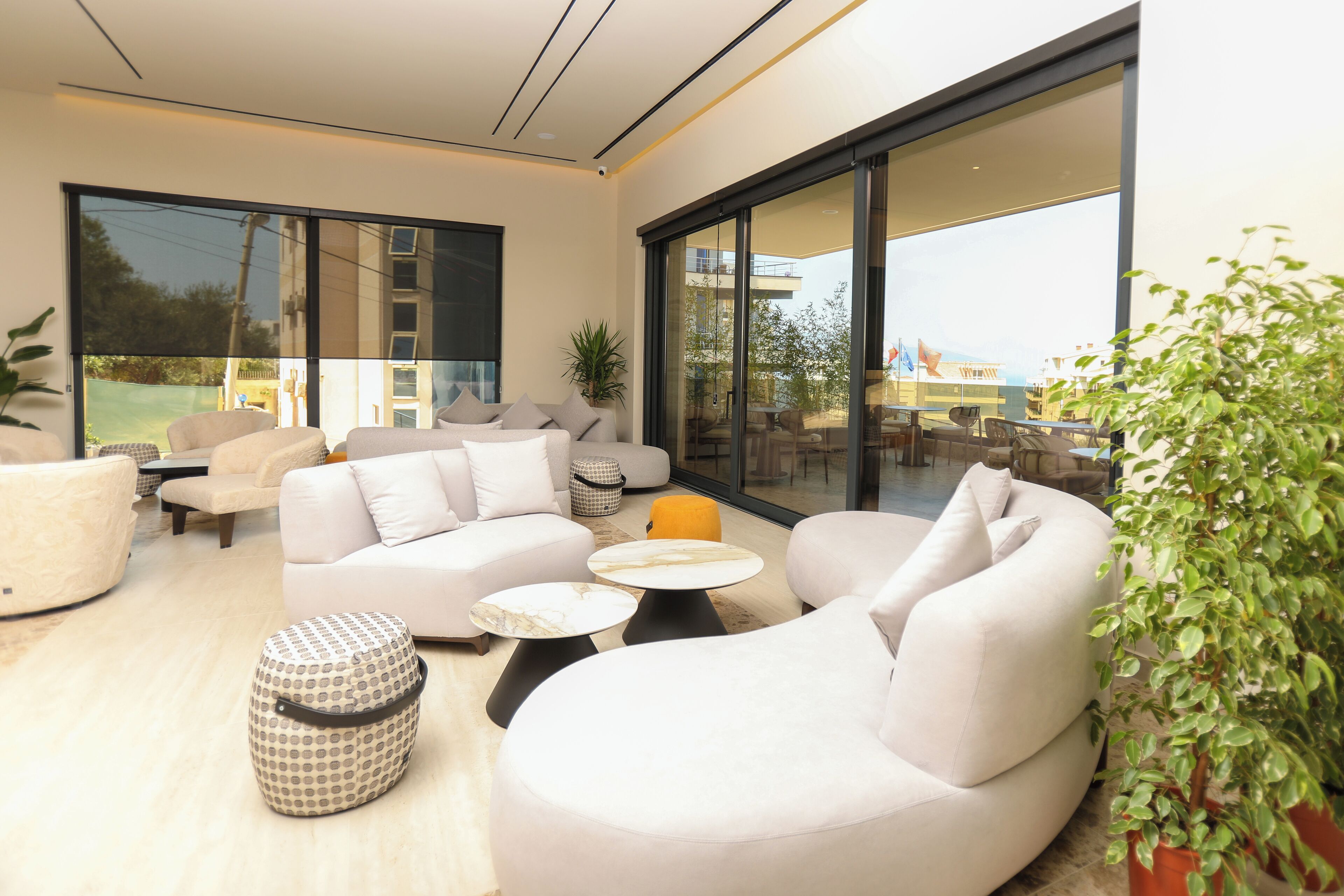 Una sala moderna con un sofá grande, una mesa de centro y un comedor visible a través de amplios ventanales.