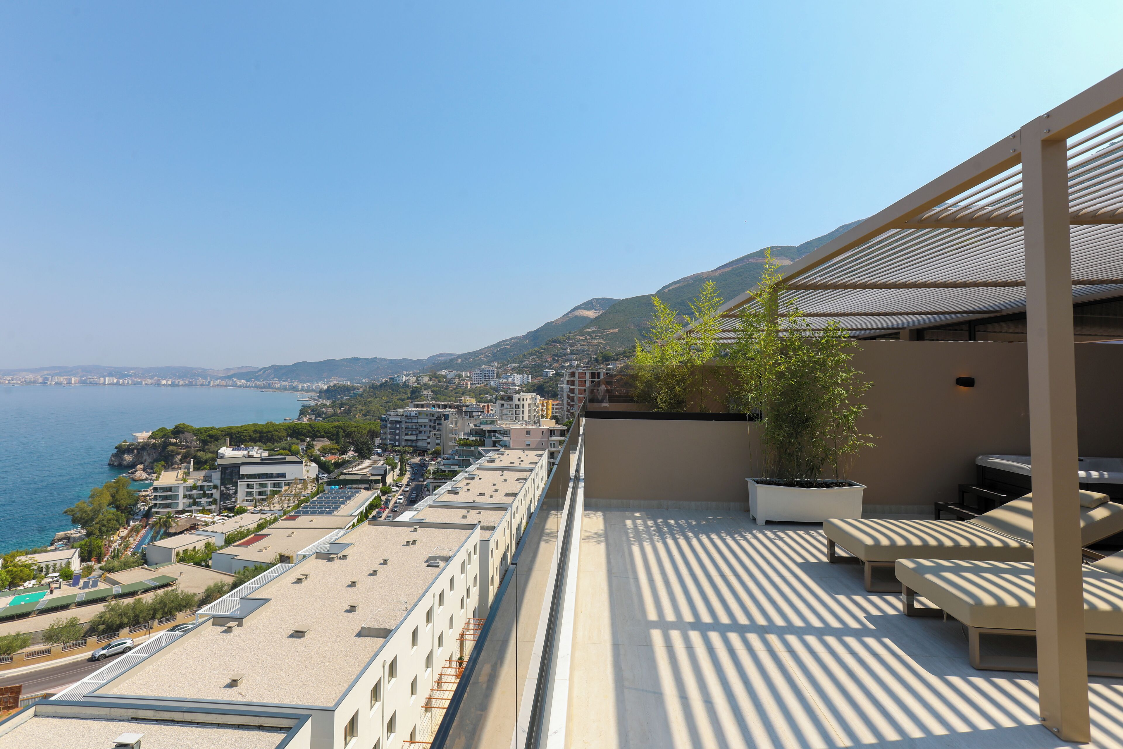 Eine Dachterrasse mit Außenmöbeln, mit Blick auf eine Küstenstadt und das Meer.