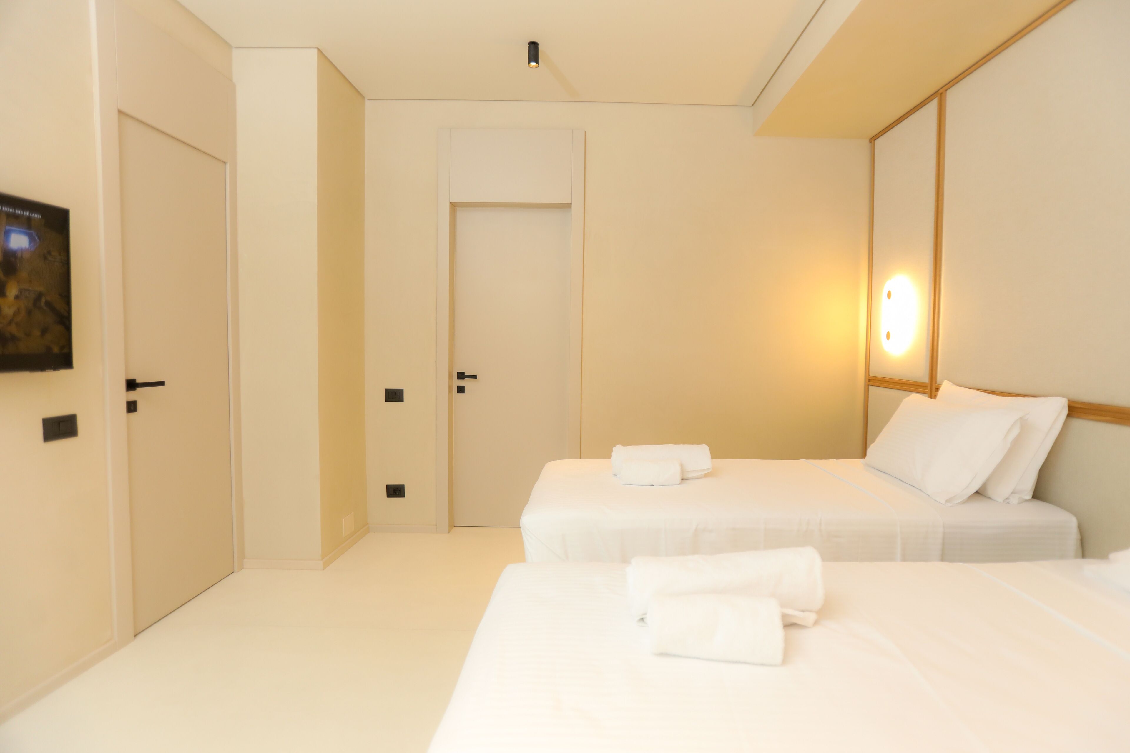 A hotel room with two beds, a door, and a wall-mounted light fixture.