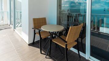 A balcony with a round table and two wicker chairs, overlooking a body of water.