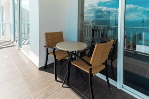 A balcony with a round table and two wicker chairs, overlooking a body of water.